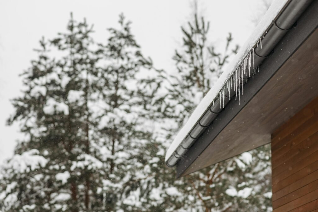 pexels photo 6667091 6667091 Stunning winter scene of icicles hanging from a snow-covered roof with snowy pines in the background.
